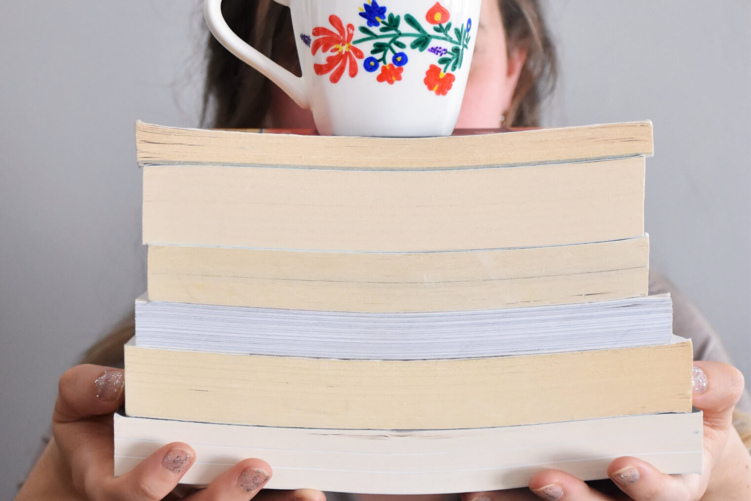 Katelyn is holding books with a ceramic cup on top.